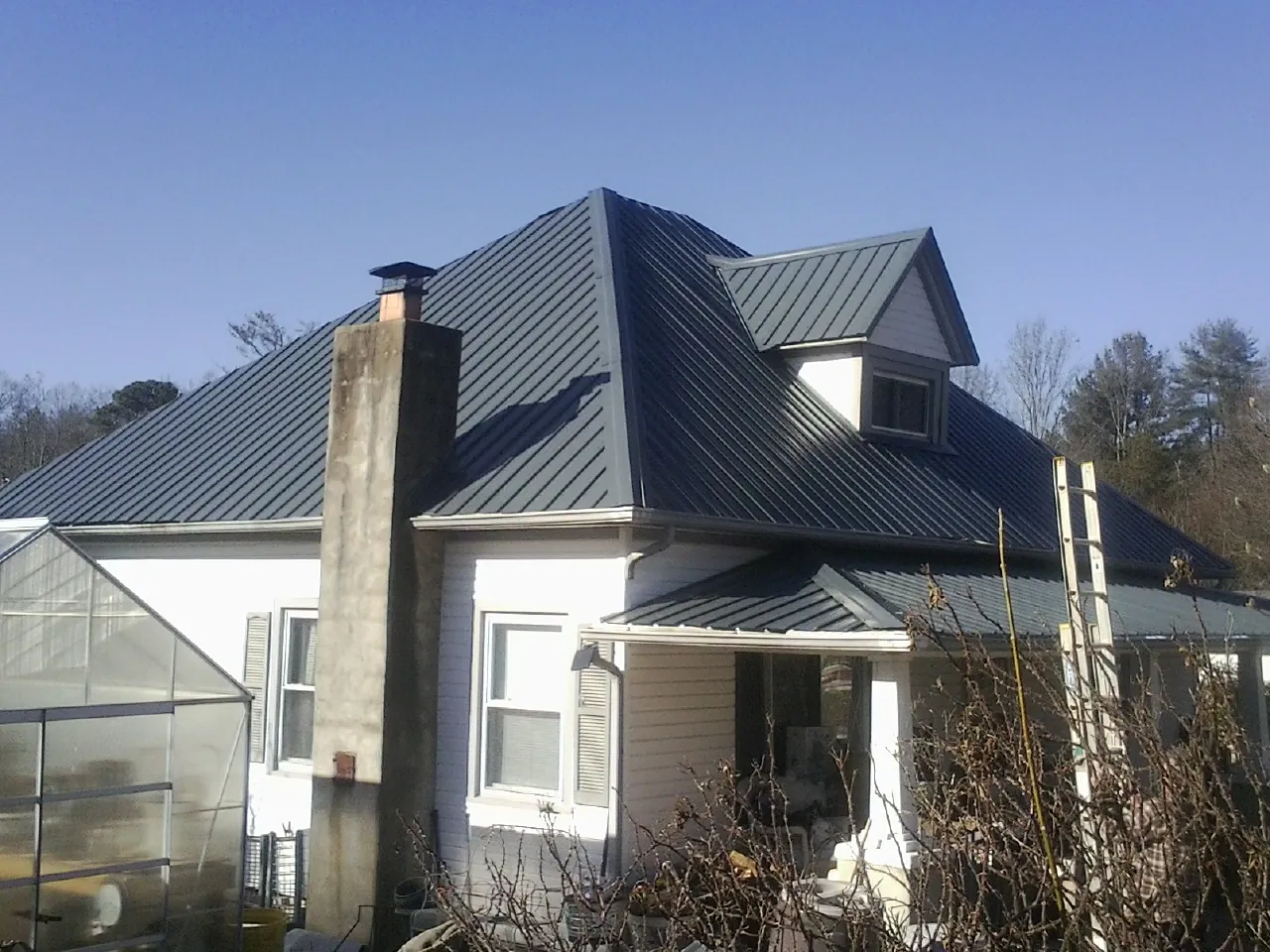Dark blue standing seam metal roof on a white farmhouse with dormer — Slate & Tile Roof Repair by Roofing Brothers in Gallatin Gateway