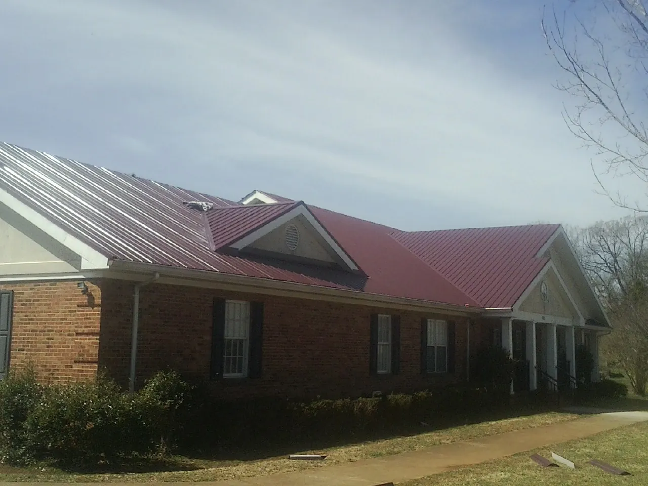 Red metal roof with gabled entries on a long brick building, from a Hail Damage Roof Repair job in Gallatin Gateway