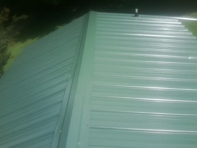 New green metal panels meeting at the ridge of a roof — Flat Roof Repair work by our crew in Gallatin Gateway