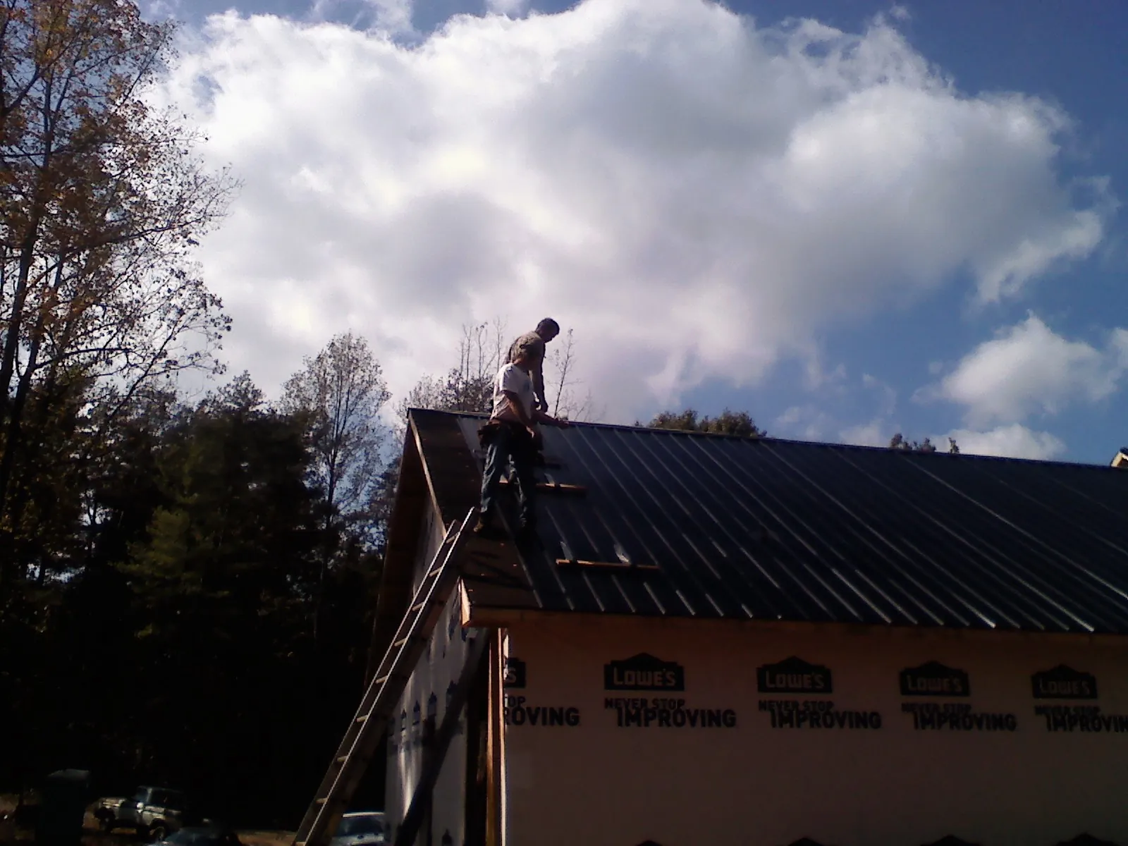 Roofer fastening dark metal panels high against a cloudy sky, from a Roof Inspection job in Gallatin Gateway