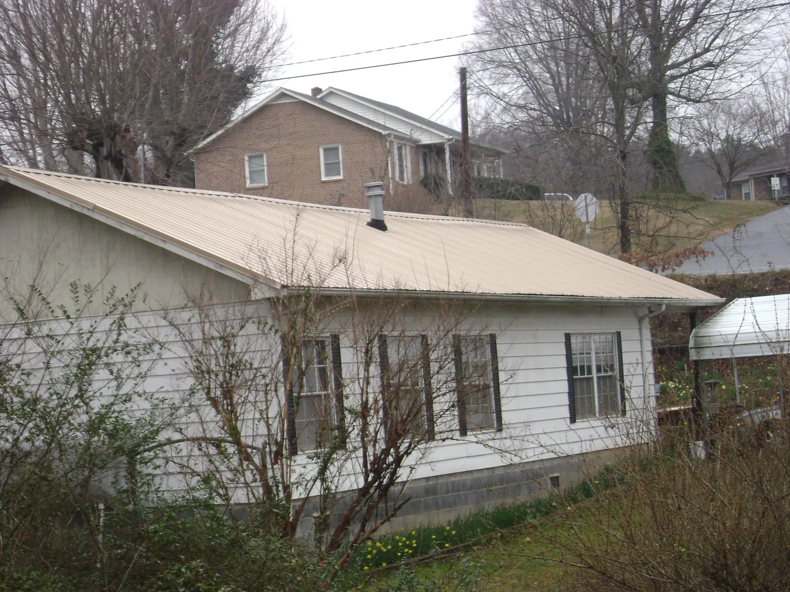 Tan metal roof on a white sided house set into a hillside — Commercial Roofing by Roofing Brothers in Gallatin Gateway