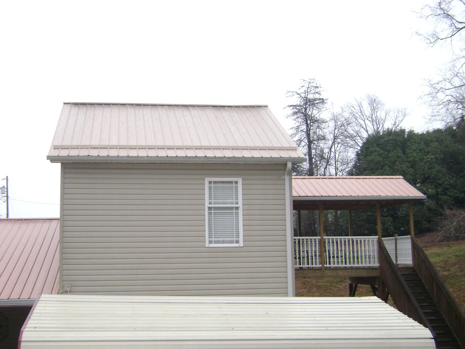 Tan metal roofs on a two story addition and attached porch, from a Roof Replacement job in Gallatin Gateway